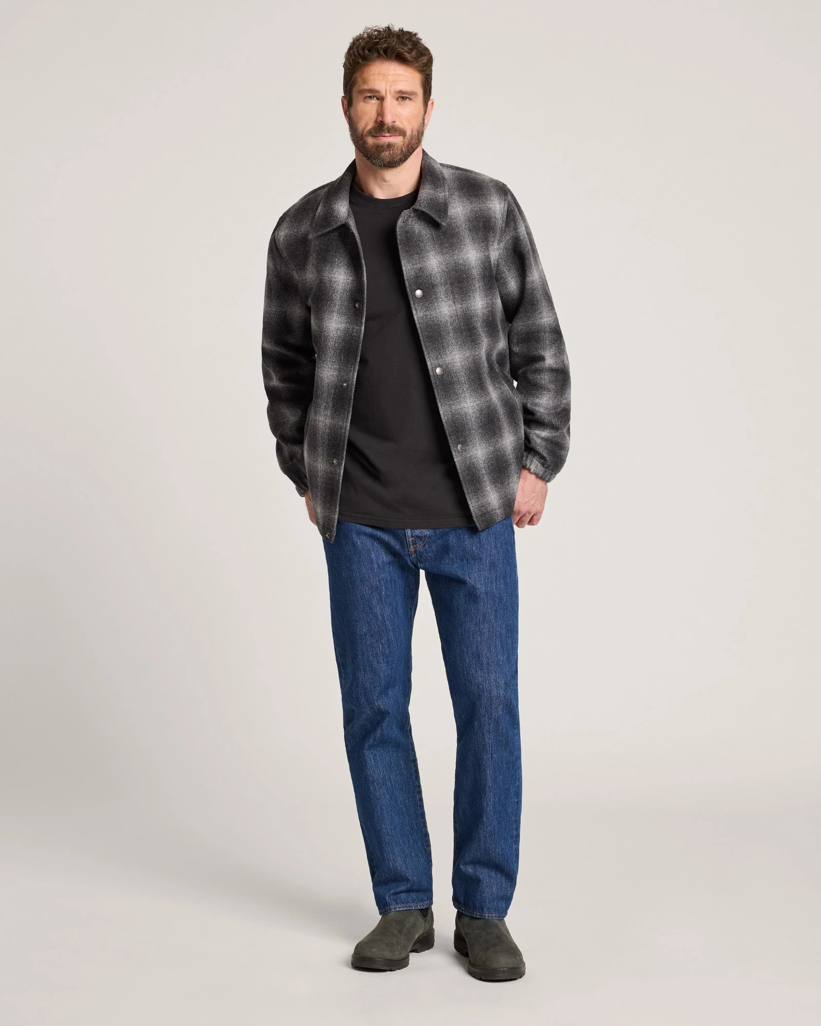 Man wearing a plaid shirt over a black t-shirt and blue jeans on a white background