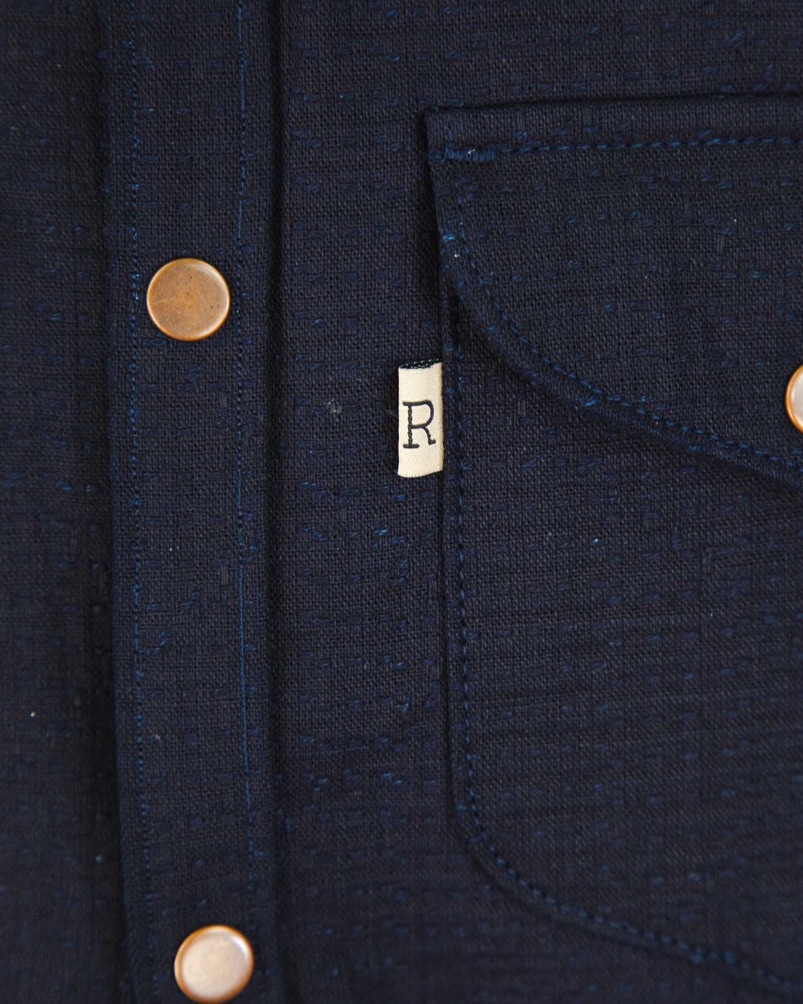 Close-up of a navy blue jacket with brass buttons and a brand logo on a dark background