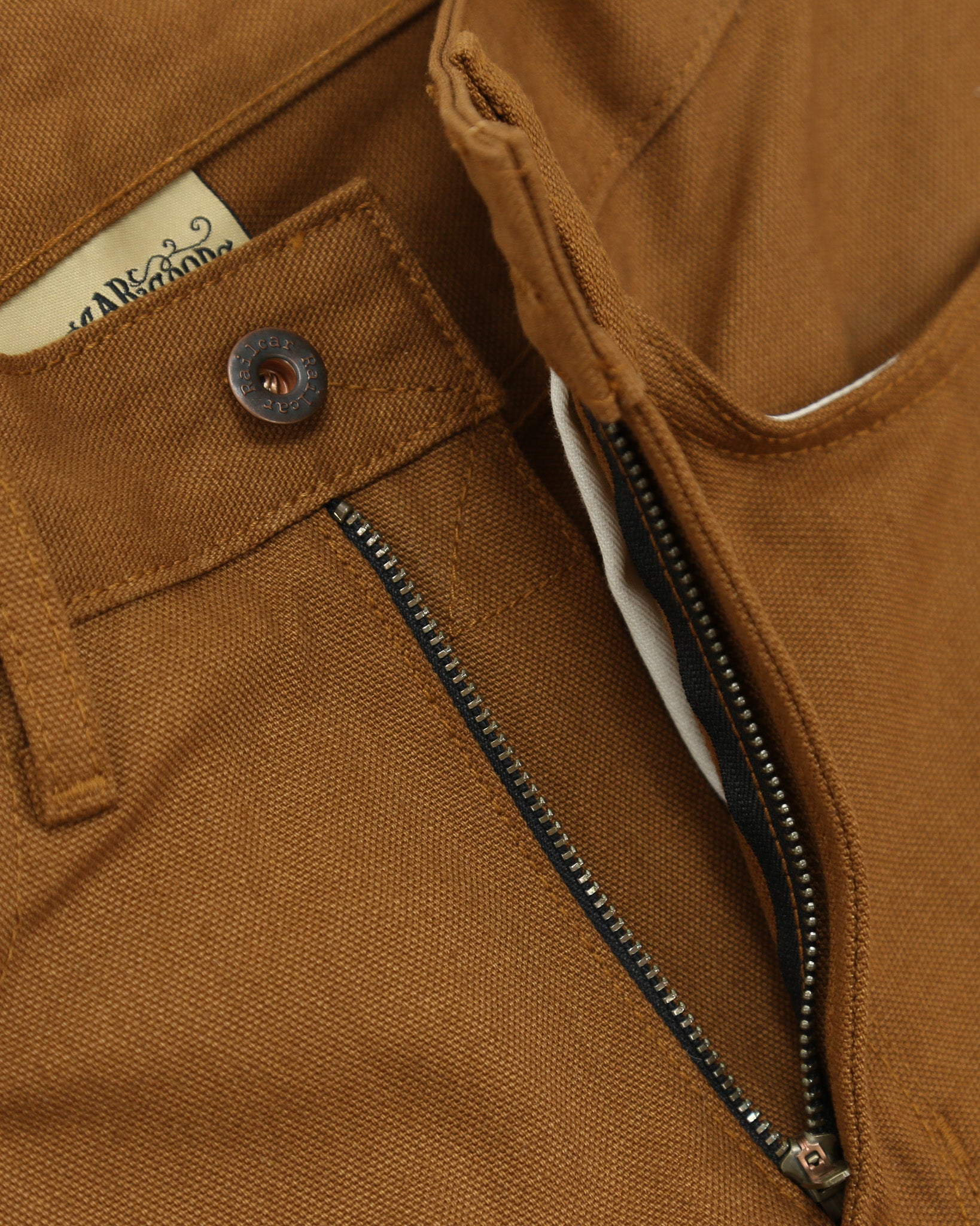 Close-up of a brown canvas pants with a zipper and button detail.