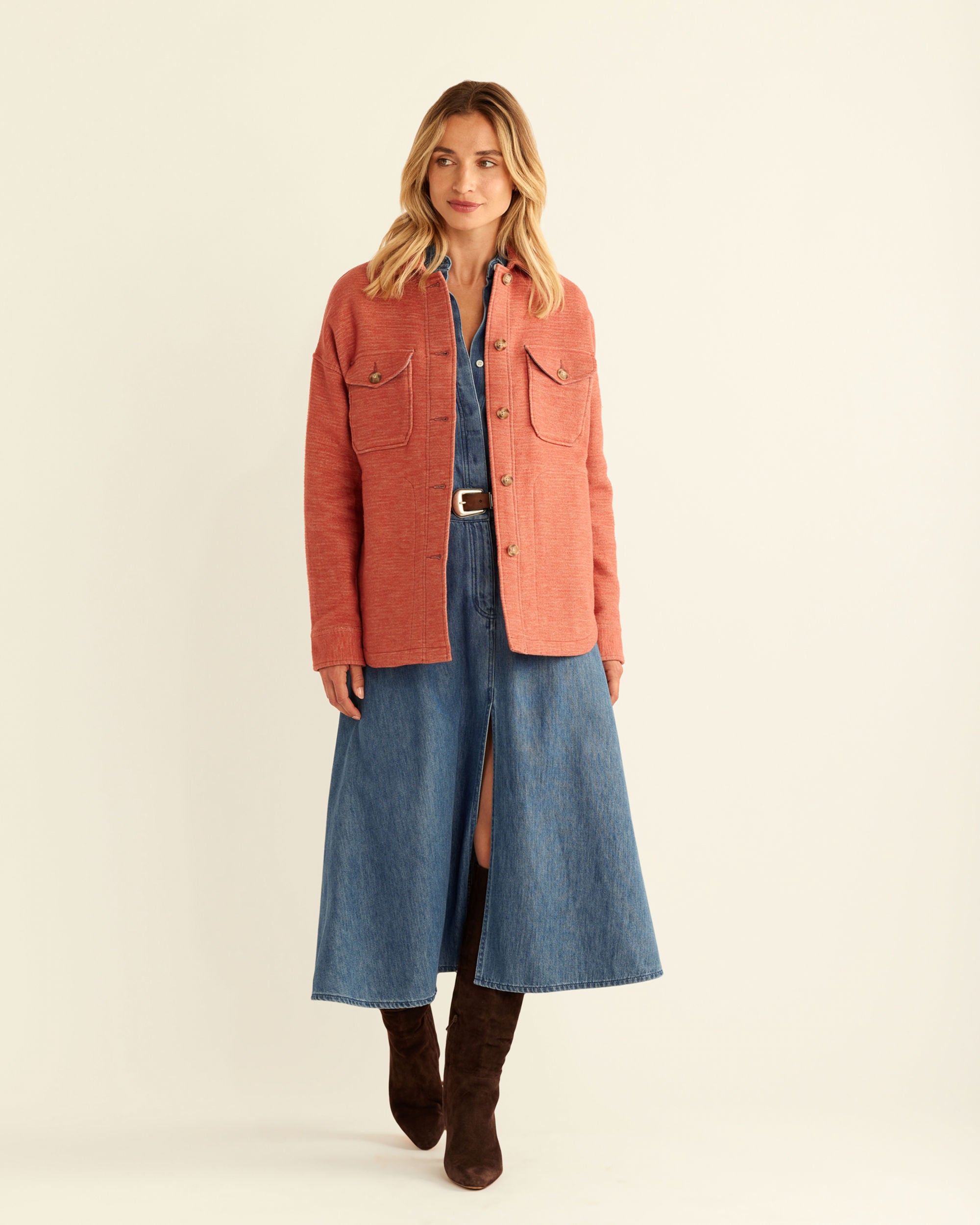 Woman wearing a red coat over a denim dress on a beige background