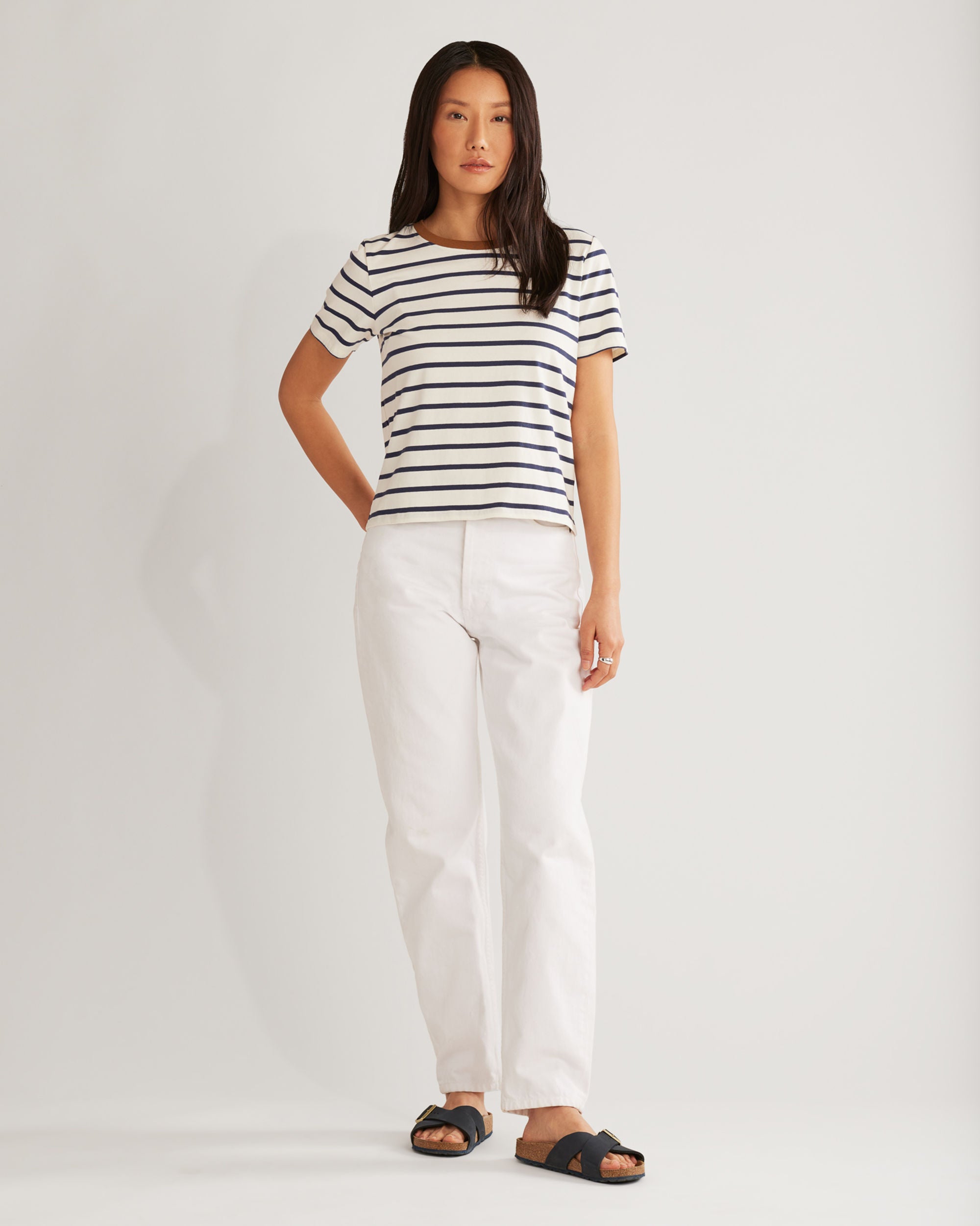 Woman wearing a striped shirt and white pants on a plain background