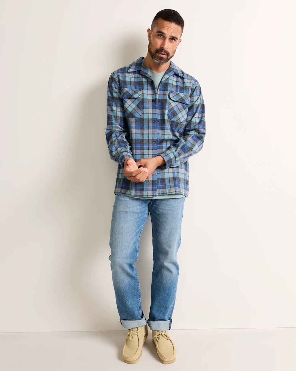 Man wearing a blue plaid shirt and jeans against a plain background