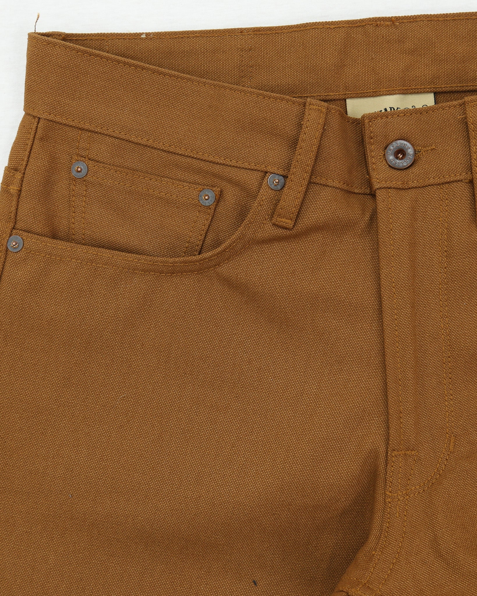 Close-up of brown canvas pants with a focus on the waistband and pocket area.