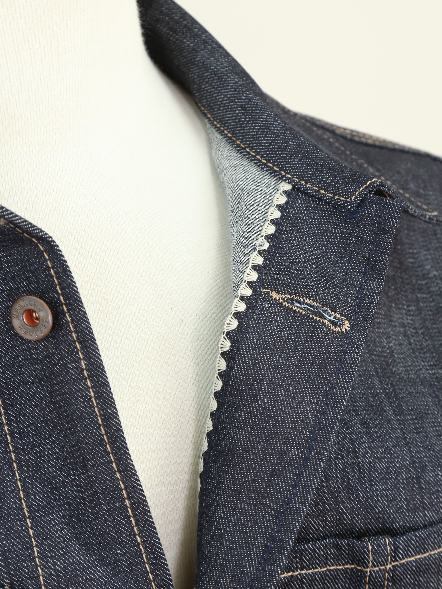 Close-up of a blue denim garment with stitching details on a white background
