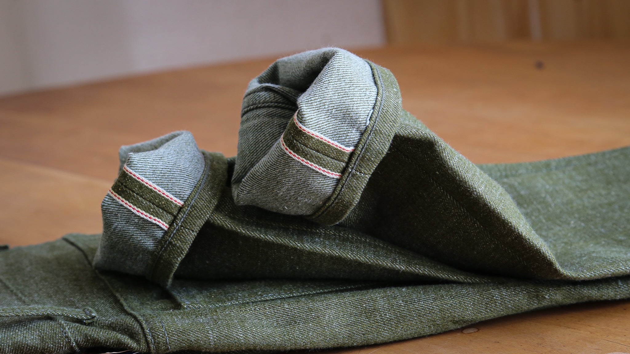 X079 Pistachio Green jeans with rolled-up cuffs on a wooden surface