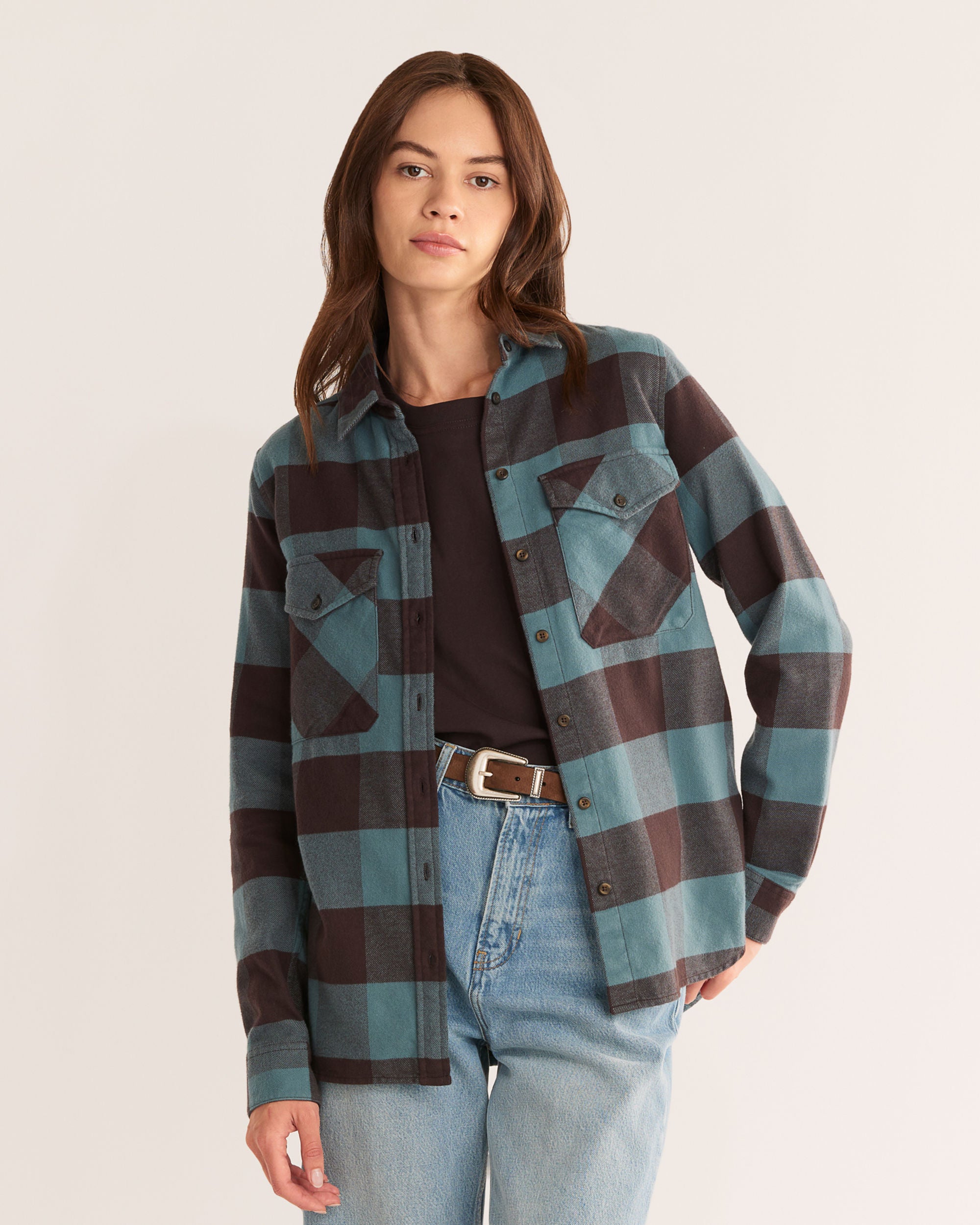 Person wearing a plaid shirt over a black top and jeans on a plain background