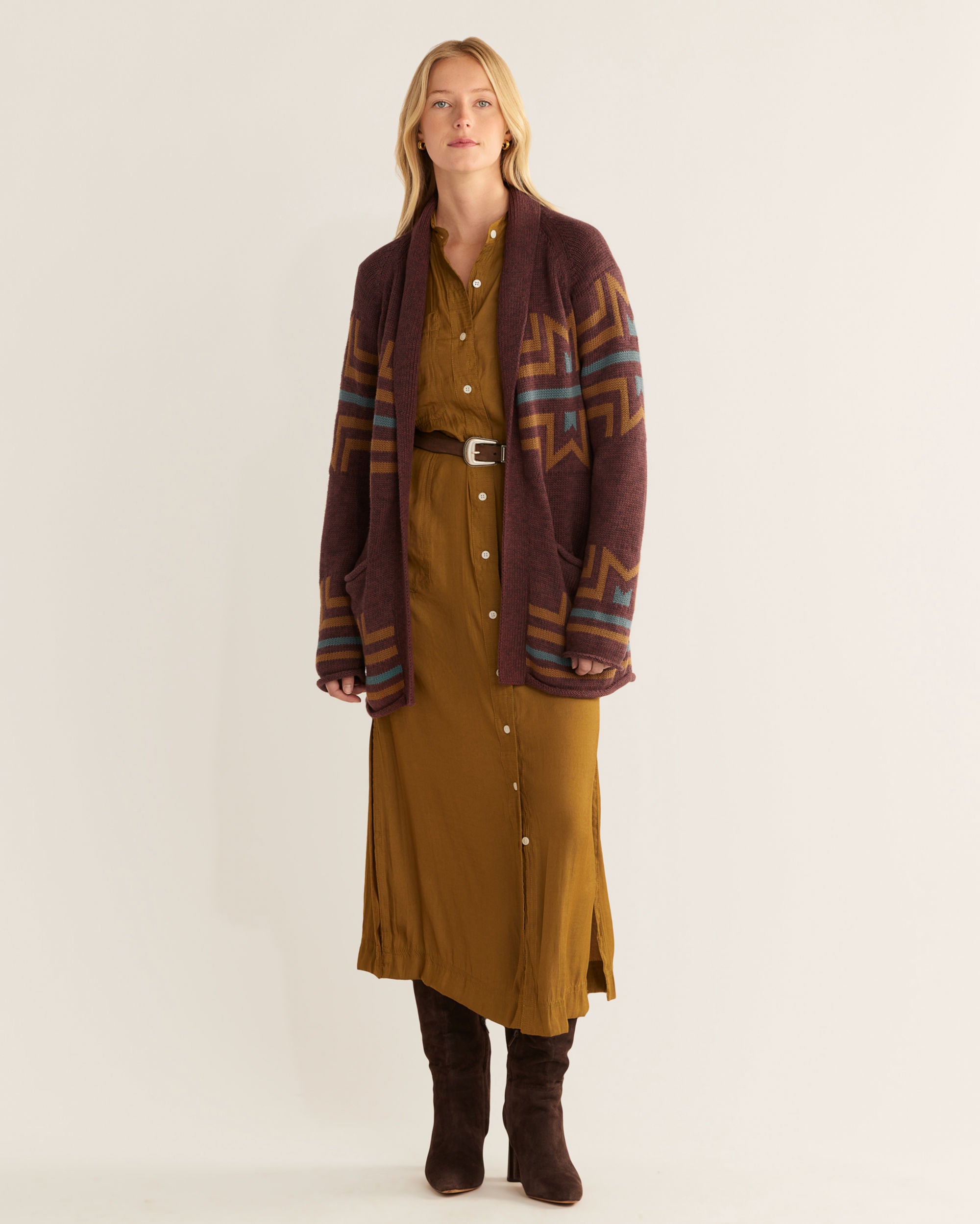 Woman wearing a long brown dress and patterned cardigan on a white background