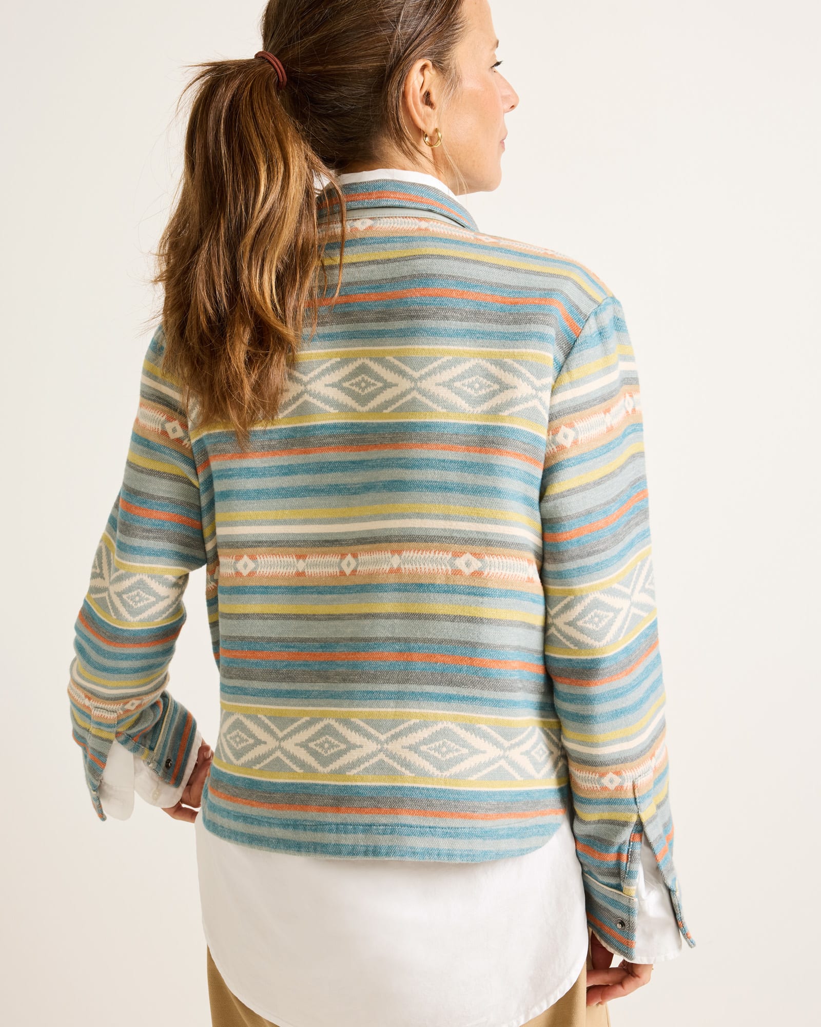 Woman wearing a colorful patterned long-sleeve shirt against a white background