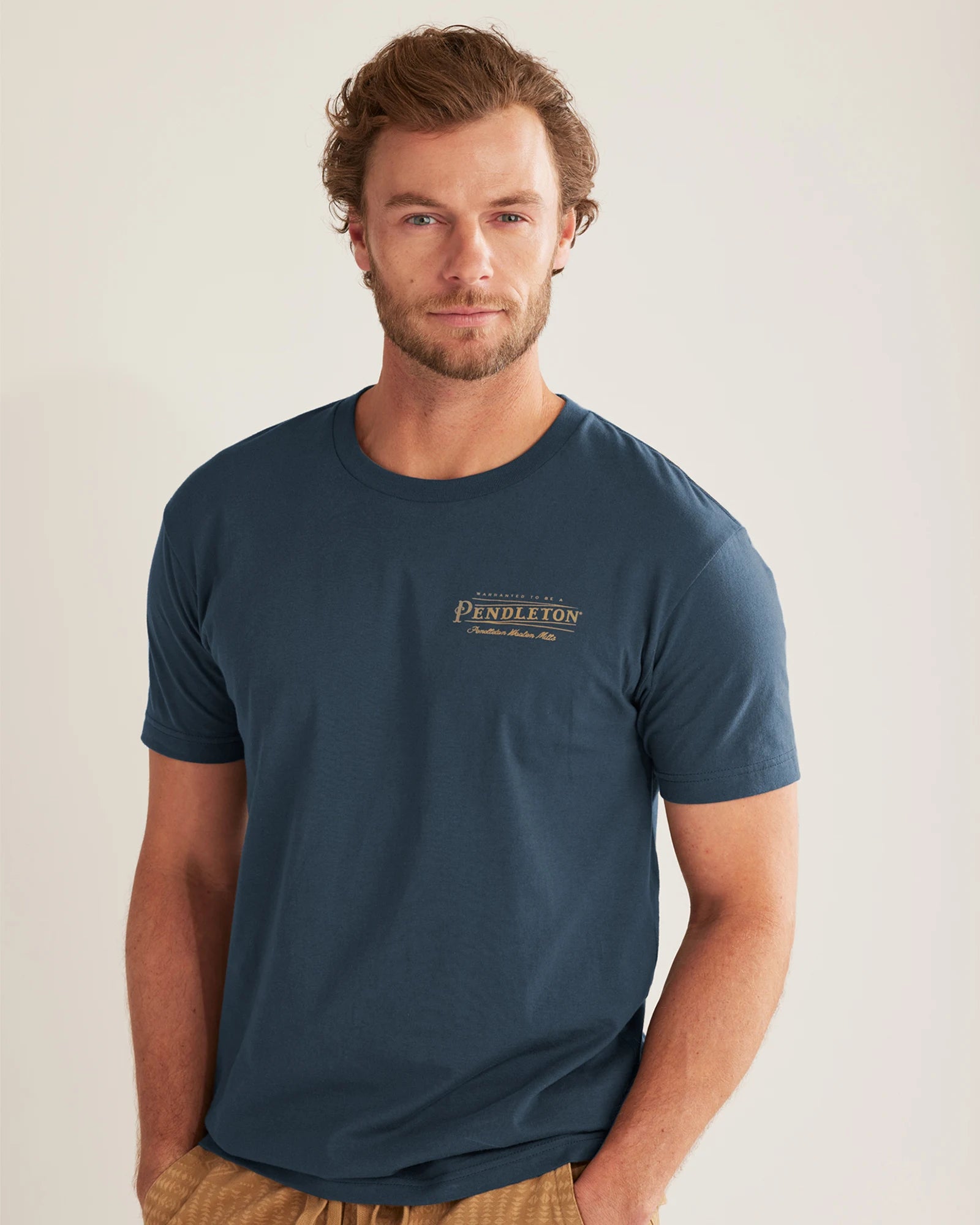 A man wearing a navy Pendleton logo graphic tee and beige shorts.