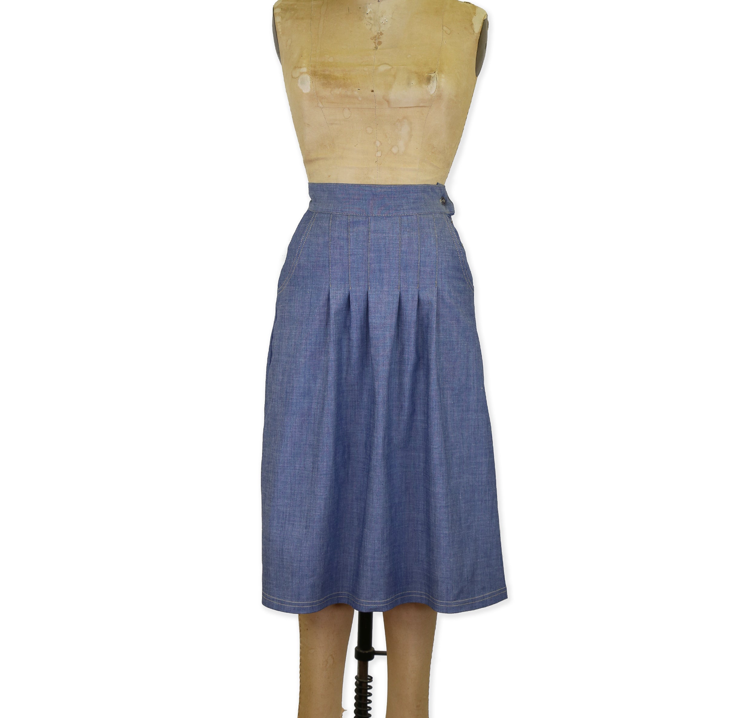 A front pleated chambray indigo skirt with side hand pockets, displayed on a mannequin.